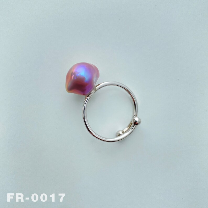 May include: A silver ring with a pink iridescent pearl. The ring has a simple design with a round pearl set on a thin band.