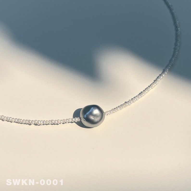 May include: A silver pearl necklace with a single large gray pearl pendant.