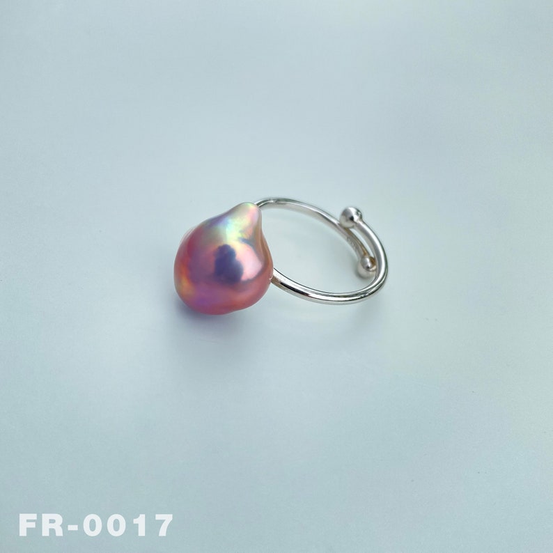May include: A silver ring with a large, pink baroque pearl. The pearl has an iridescent sheen.