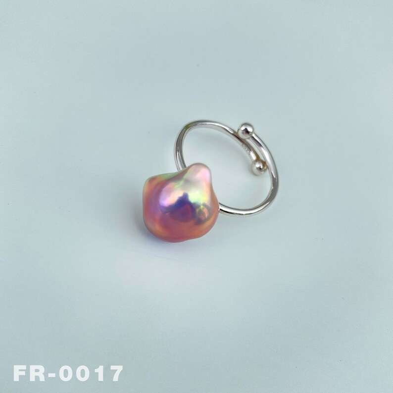 May include: A silver ring with a large, iridescent pink pearl. The ring is open and adjustable.