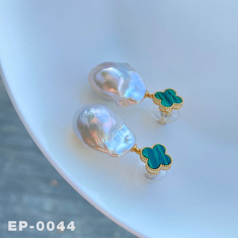 May include: A pair of earrings featuring large, white baroque pearls with a green malachite clover charm. The earrings are gold-toned and have a post back.
