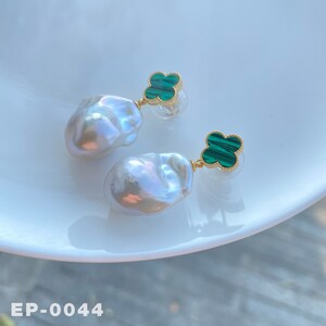 May include: A pair of earrings with white baroque pearls and green malachite clover charms. The earrings are on a white surface with the text "EP-0044".