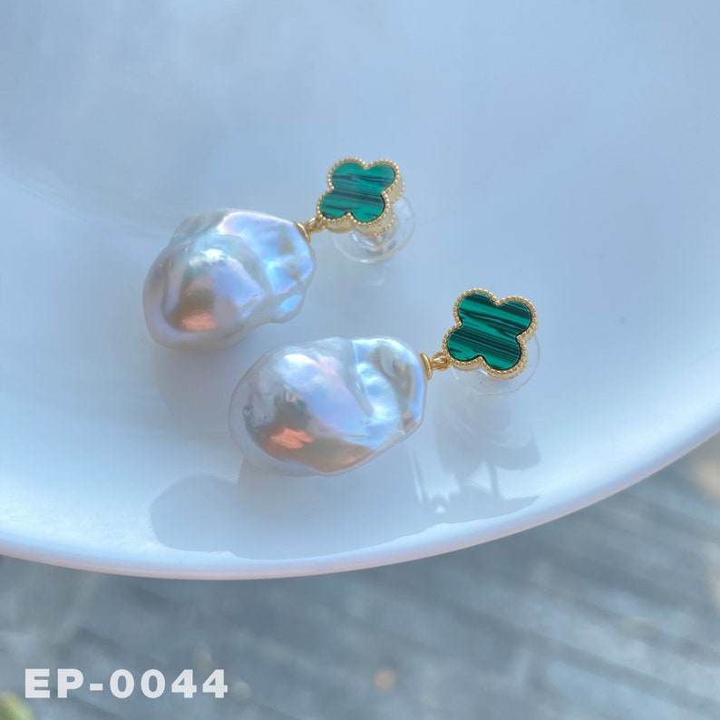 May include: A pair of earrings with white baroque pearls and green malachite clover charms. The earrings are on a white surface with the text "EP-0044".