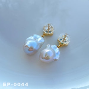 May include: A pair of gold earrings with white baroque pearls and green gemstones. The earrings have a delicate floral design.