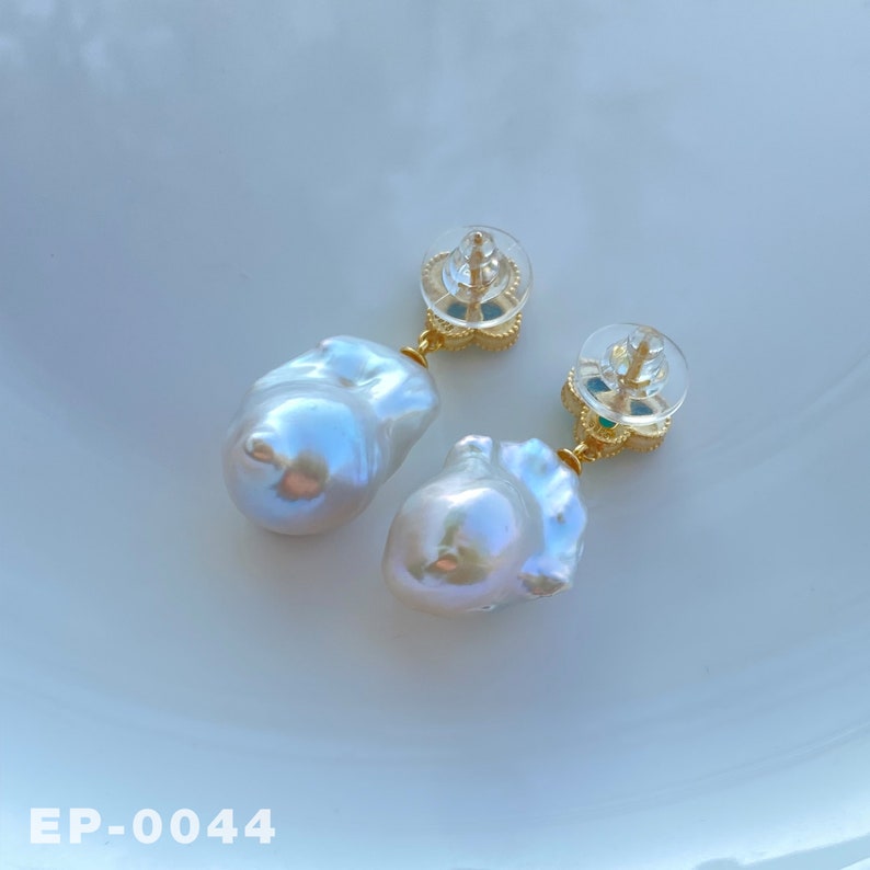 May include: A pair of gold earrings with white baroque pearls and green gemstones. The earrings have a delicate floral design.