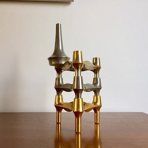 Op de afbeelding: Een gouden en zilveren kandelaar met een modern ontwerp. De kandelaar heeft meerdere armen en een hoge, puntige top.