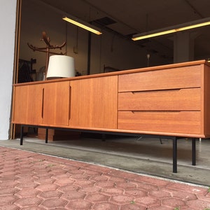 May include: A mid-century modern teak sideboard with three drawers and two doors. The sideboard has black metal legs and is in good condition.