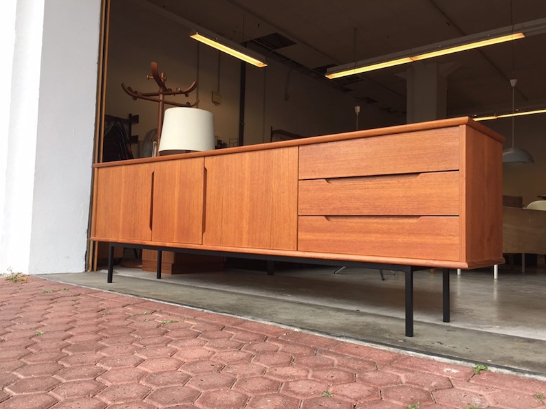 May include: A mid-century modern teak sideboard with three drawers and two doors. The sideboard has black metal legs and is in good condition.