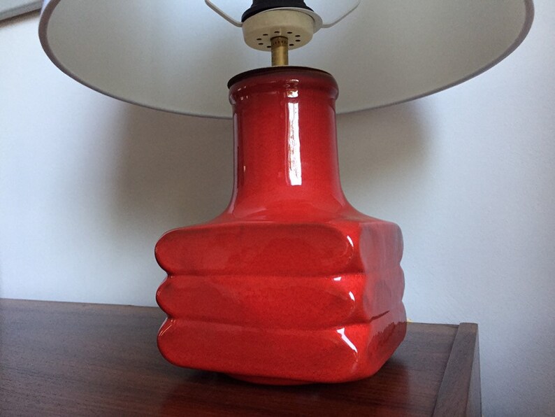 May include: A red ceramic table lamp with a white lampshade. The lamp base has a unique, layered design.