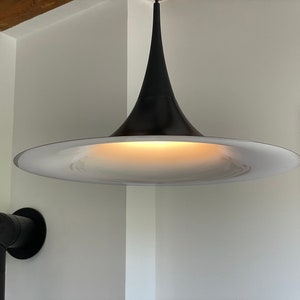 May include: A black and white modern pendant light fixture with a wide, circular, white shade and a black, cone-shaped top.