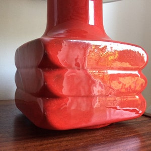 May include: A red ceramic table lamp with a square base and a rounded top. The lamp has a glossy finish and a unique, layered design.