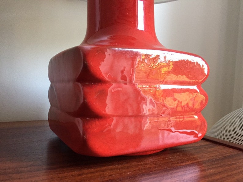 May include: A red ceramic table lamp with a square base and a rounded top. The lamp has a glossy finish and a unique, layered design.
