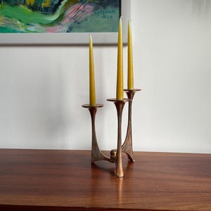 Op de afbeelding: Een gouden metalen kandelaar met drie armen en drie gele kaarsen.