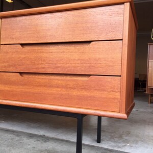 May include: A mid-century modern dresser with three drawers and black metal legs. The dresser is made of wood with a rich brown finish.