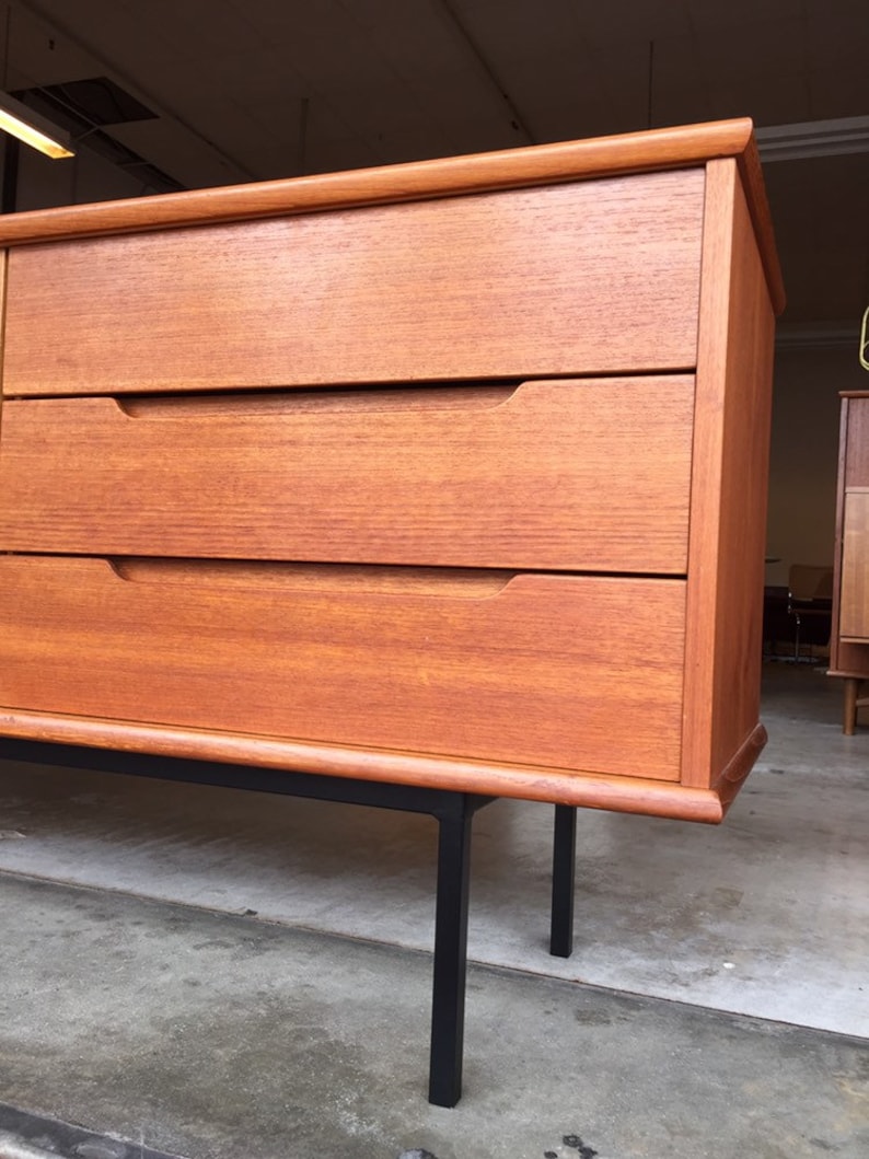 May include: A mid-century modern dresser with three drawers and black metal legs. The dresser is made of wood with a rich brown finish.