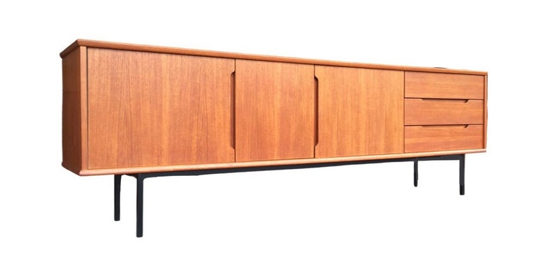 May include: A mid-century modern teak sideboard with three doors and two drawers. The sideboard has black metal legs and a light wood finish.