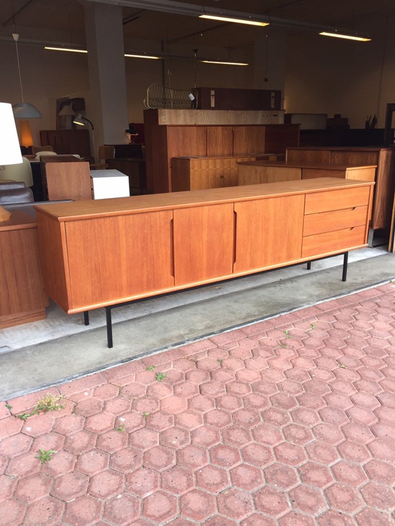 May include: A mid-century modern teak sideboard with four doors and three drawers. The sideboard has black metal legs and is in good condition.