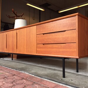 May include: A mid-century modern teak sideboard with three drawers and two doors. The sideboard has black metal legs and is in good condition.