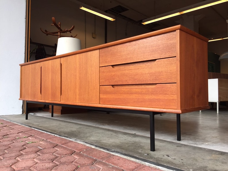 May include: A mid-century modern teak sideboard with three drawers and two doors. The sideboard has black metal legs and is in good condition.