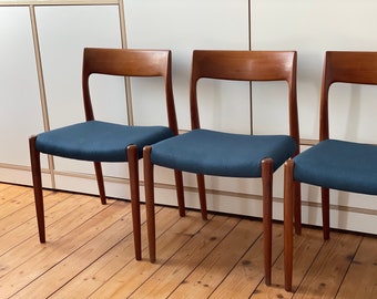 Puede incluir: Tres sillas de madera con asientos de tela azul oscuro. Las sillas tienen un diseño sencillo y moderno de mediados de siglo.