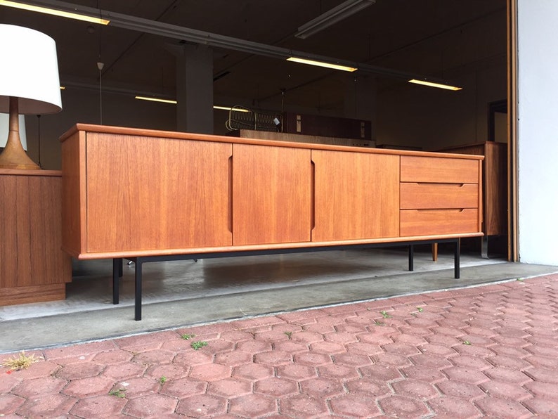 May include: A mid-century modern teak sideboard with four doors and two drawers. The sideboard has black metal legs and is in good condition.
