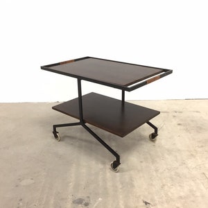Könnte beinhalten: Ein zweistöckiger Servierwagen mit einem schwarzen Metallrahmen und dunklen Holzböden. Der Wagen hat vier Räder und ist ideal zum Servieren von Getränken und Snacks.