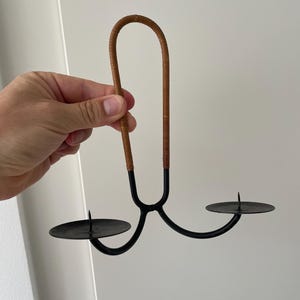 Op de afbeelding: Een zwarte metalen kaarsenhouder met twee kaarsbekers en een bruine leren band om op te hangen.