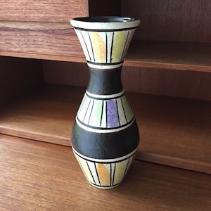 May include: A black ceramic vase with a geometric design in white, yellow, green, and purple. The vase has a narrow neck and a rounded body.