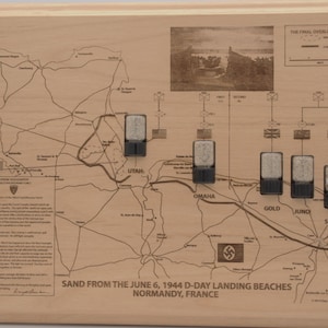 May include: A rectangular wooden plaque featuring an engraved map of Normandy, France, detailing the June 6, 1944 D-Day landing beaches. It includes five small, clear containers filled with sand from Utah, Omaha, Gold, Juno, and Sword beaches.