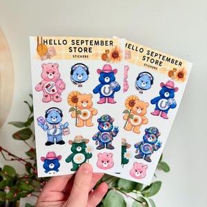 May include: Two sticker sheets with cartoon bears in various outfits and accessories. The stickers include bears with headphones, cowboy hats, and sunflowers. The text "HELLO SEPTEMBER STORE" and "STICKERS" is printed at the top of each sheet.