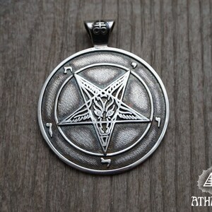 May include: A silver pendant featuring a pentagram with a goat's head inside, surrounded by a circle with Hebrew characters.
