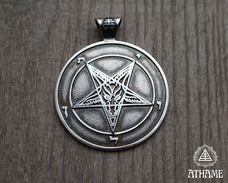 May include: A silver pendant featuring a pentagram with a goat's head inside, surrounded by a circle with Hebrew characters.