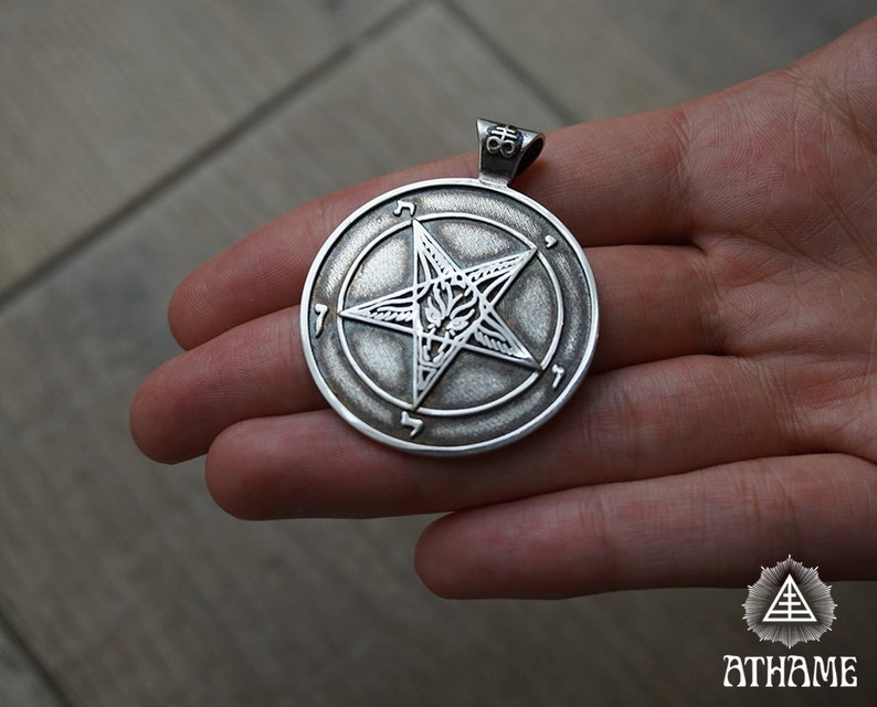 May include: Silver pendant featuring a pentagram with a goat's head inside. The pentagram is surrounded by a circle with the numbers 1-6 inscribed around it.