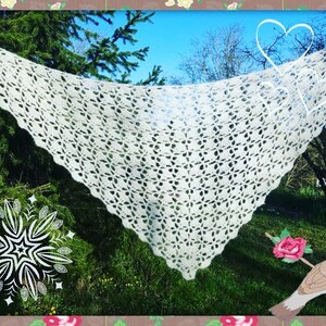 May include: A white crocheted shawl with a delicate openwork pattern, draped over a tree branch in a garden setting.