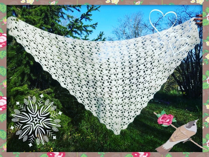 May include: A white crocheted shawl with a delicate openwork pattern, draped over a tree branch in a garden setting.