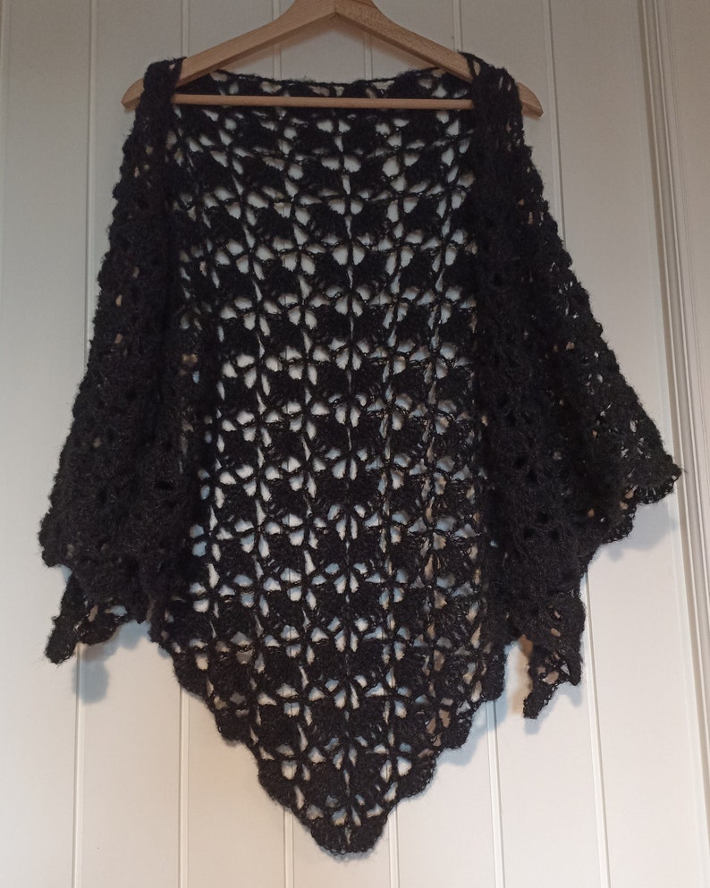 May include: A black crocheted shawl with a delicate openwork pattern. The shawl is draped over a wooden hanger.