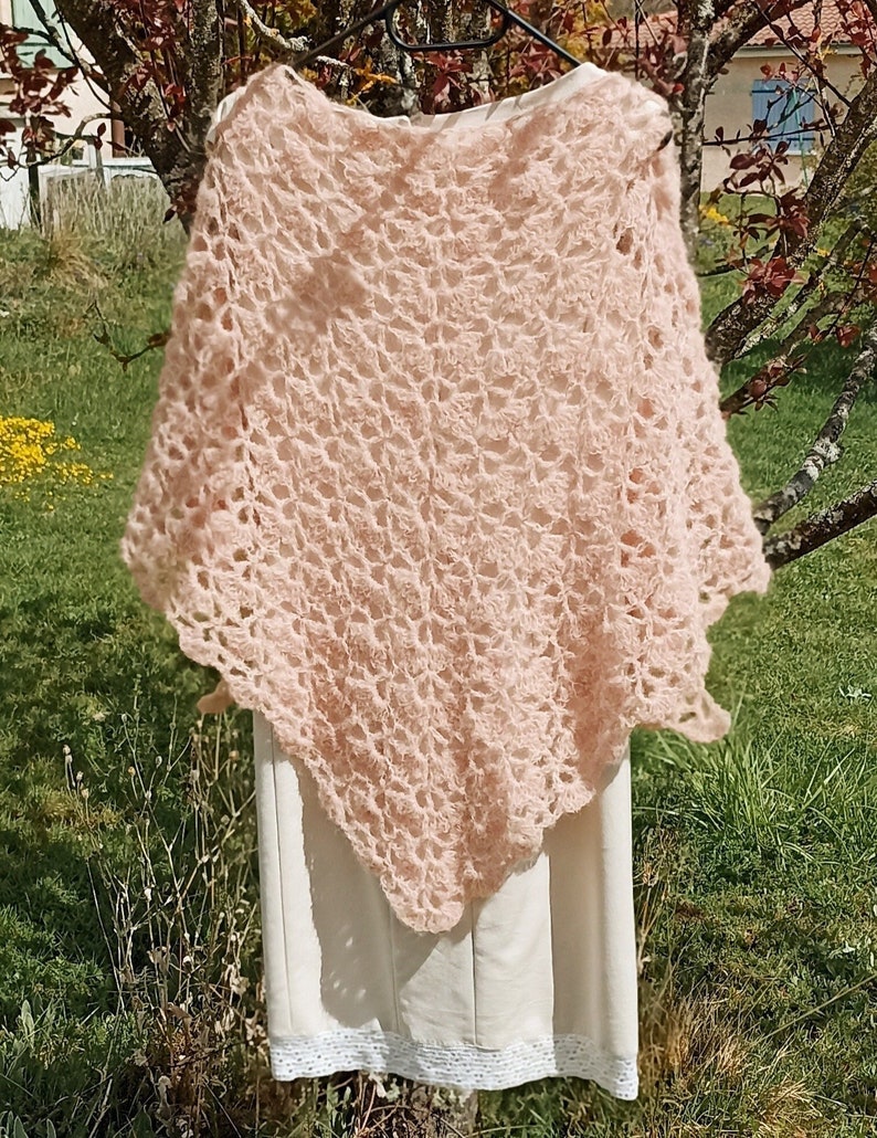 May include: A delicate, crocheted shawl in a soft pink color. The shawl is made with a lacy pattern and has a slightly scalloped edge.
