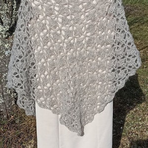 May include: A gray crocheted shawl with a delicate openwork pattern. The shawl is draped over a white dress with a lace trim.