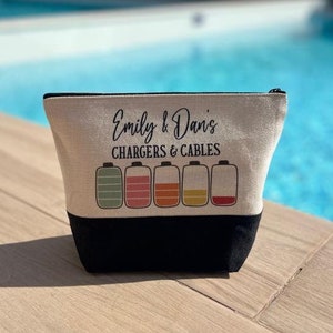 May include: A beige canvas zippered pouch with black trim. The pouch has the text "Emily & Dan's Chargers & Cables" printed on it. There are five battery icons with different colored levels printed on the pouch.