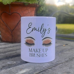 May include: White ceramic mug with the text "Emily's Make Up Brushes" and a graphic of two eyes with gold glitter eyeshadow.