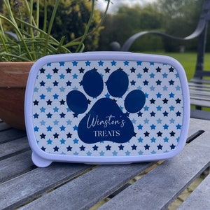May include: White rectangular lunchbox with a blue paw print and blue stars on a white background. The paw print has the text "Winston's Treats" inside.