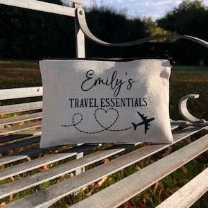 May include: A beige canvas travel pouch with black trim and the text "Emily's Travel Essentials" with a heart and airplane design.