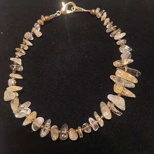 May include: A delicate gold and clear crystal bracelet with a clasp closure. The bracelet is made with small, irregular shaped crystals and gold beads.
