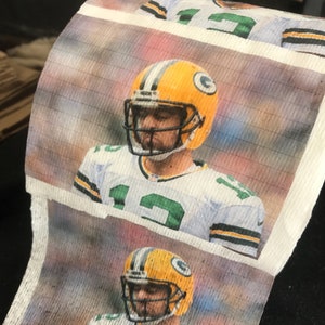 May include: A roll of toilet paper featuring a repeated image of a football player wearing a green and yellow jersey and helmet. The player is looking down and the background is blurred.