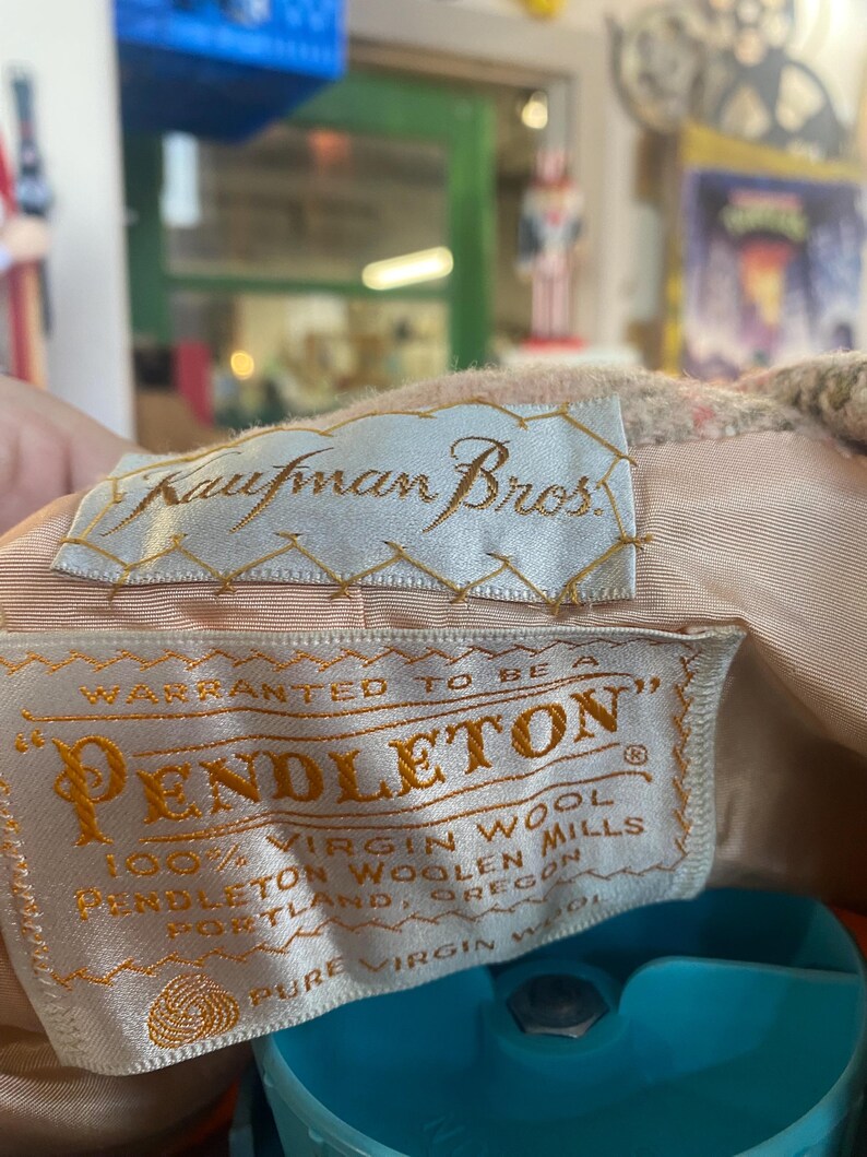 May include: Close-up of two vintage fabric labels. The top label reads "Kaufman Bros." in elegant script. The bottom label says "Pendleton" with "100% Virgin Wool" and "Pendleton Woolen Mills, Portland, Oregon" printed on it.