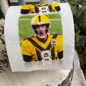 May include: A roll of white toilet paper featuring a printed image of a football player in a yellow and black uniform. The player is wearing a helmet and the number 8 is visible on the jersey.