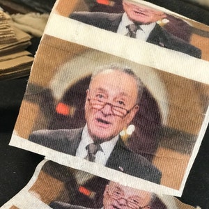 May include: A roll of toilet paper with a photo of a man in a suit and tie. The photo is printed on the toilet paper.