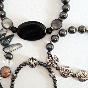 May include: Four bracelets with different styles and colors. One bracelet has black and silver beads, another has black and silver beads with a large black oval bead, another has black and silver beads with a silver charm, and the last one has iridescent beads with a silver clasp.