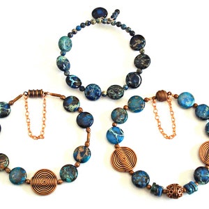 May include: Three blue and brown patterned stone bead necklaces with copper accents. The necklaces have a clasp closure and are different lengths.