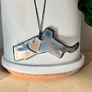May include: A ceramic ornament shaped like the state of Massachusetts with a small heart in the center. The ornament is painted in shades of blue and silver with a metallic finish.
